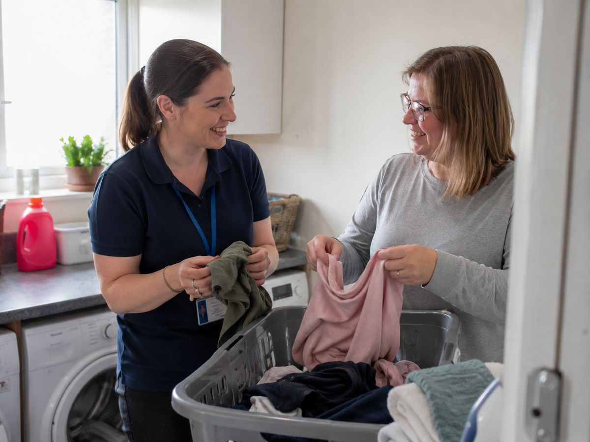 A support worker and a woman sorting laundry together in a kitchen