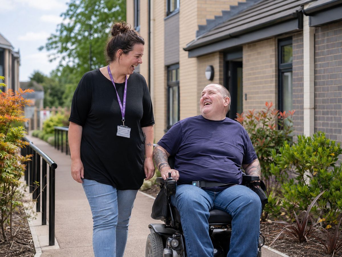 A support worker walking outdoors alongside a man using a powered wheelchair