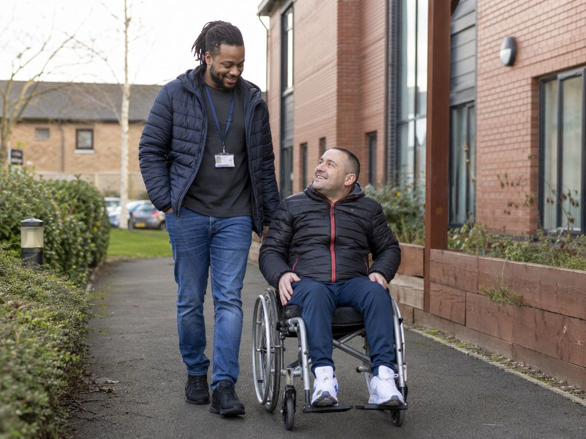 A support worker walking outdoors alongside a man using a wheelchair
